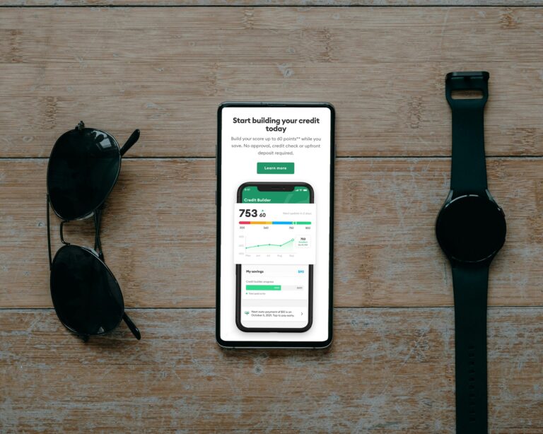 Credit score displaying on iphone next to sunglasses and a watch on wood background.